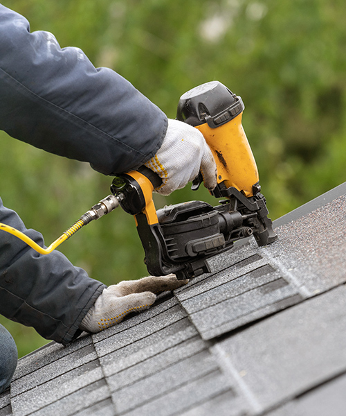 contractor hand with nailgun close up installing asphalt shingles as replacement beaverton or
